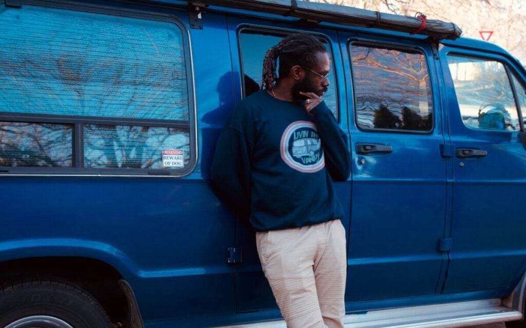 A man leans against a blue campervan as he looks away