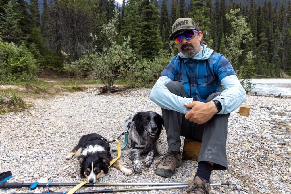 A man sitting down with two black and white dogs sitting next to him. He is in Yoho National Park