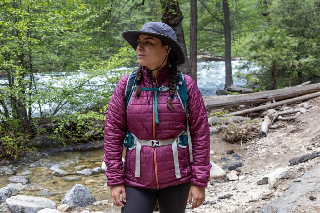 Woman hiking along a river in the forest wearing the Patagonia Quandary Brimmer sun hat and Nano Puff jacket