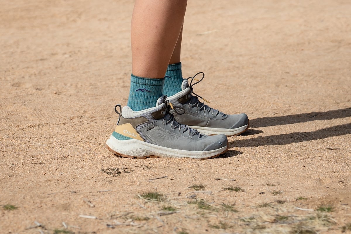 A female hiker wearing Darn Tough socks and the Oboz Cottonwood mid waterproof hiking boots in the color Drizzle on a trail in Joshua Tree National Park