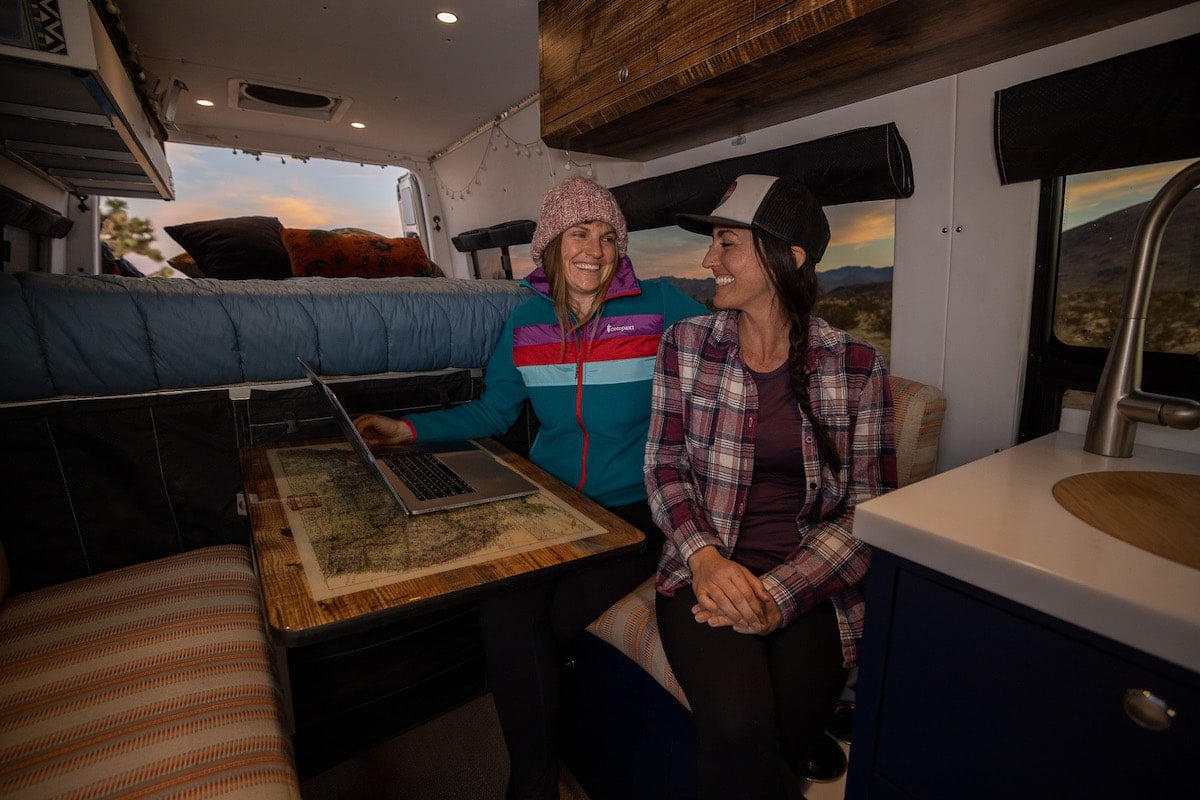 Bearfoot Theory founder Kristen Bor talking with a friend inside of a Sprinter Van with a laptop on the table