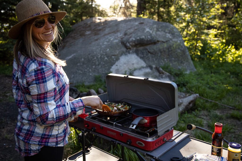 A woman cooking over a camp stove in the woods