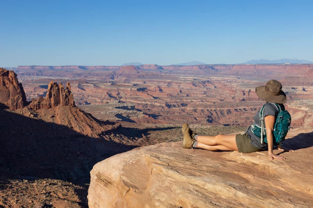 A woman sits at a lookout over Island In The Sky, Canyonlands National Park Utah. She's wearing the North Face Aphrodite Motion Shorts