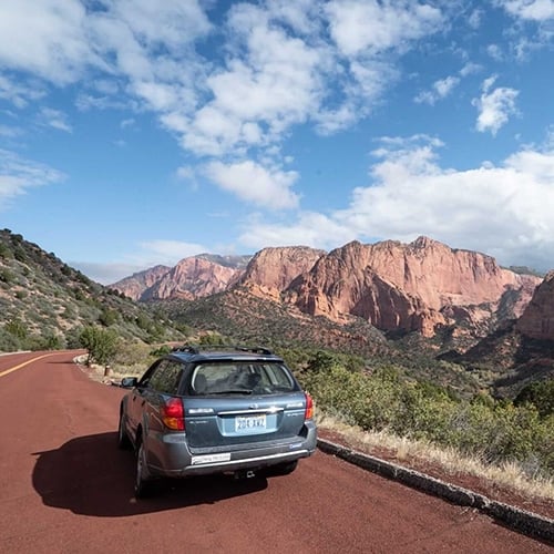 Subaru parked on the side of the road in Zion National Park with red rocks in the background