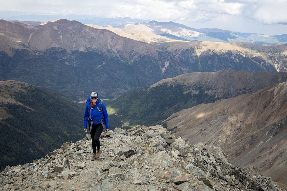 Woman hiking at high elevation on a rocky trail with mountain peaks in the background