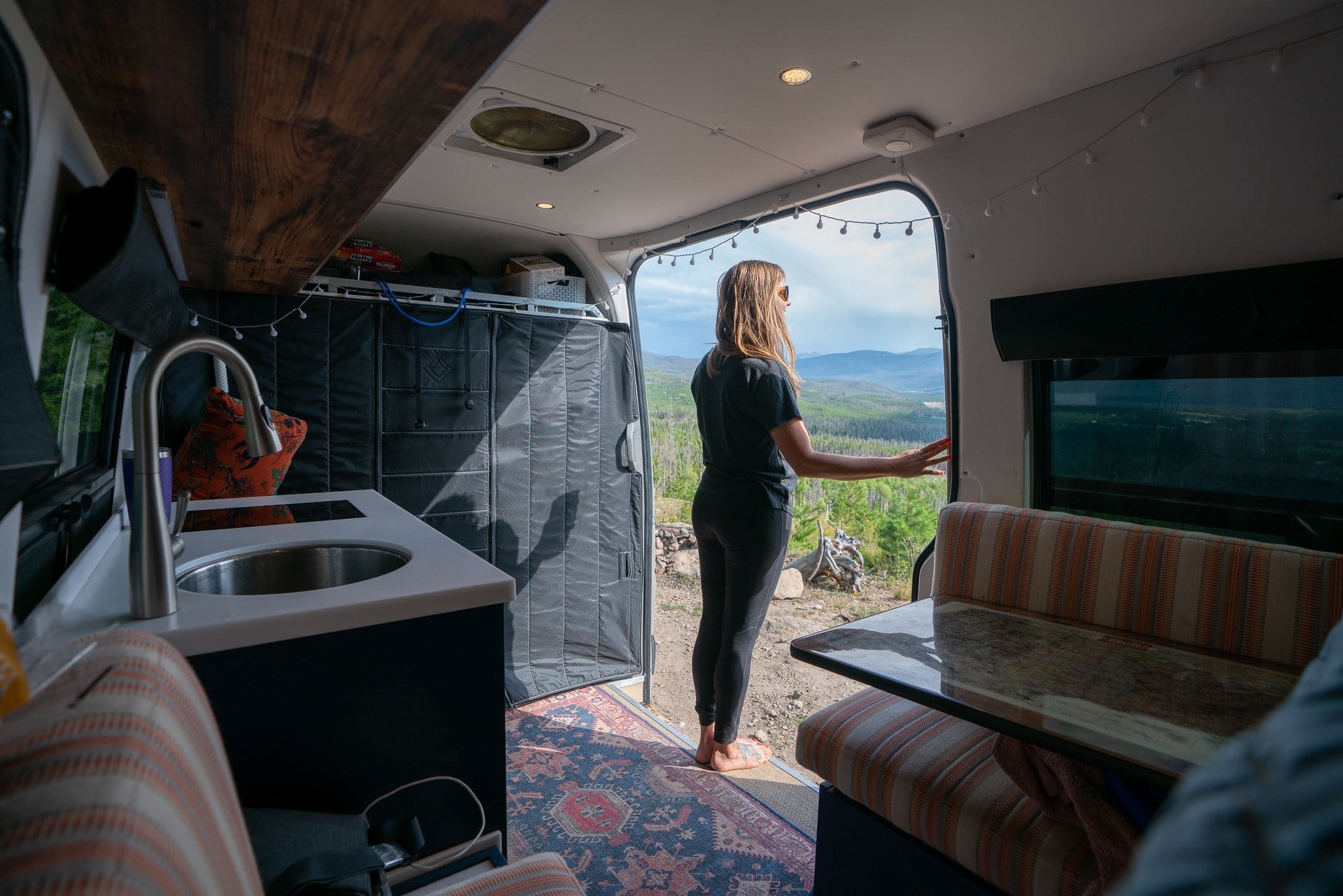 Woman standing in the doorway of a sprinter van looking out on the rolling mountains