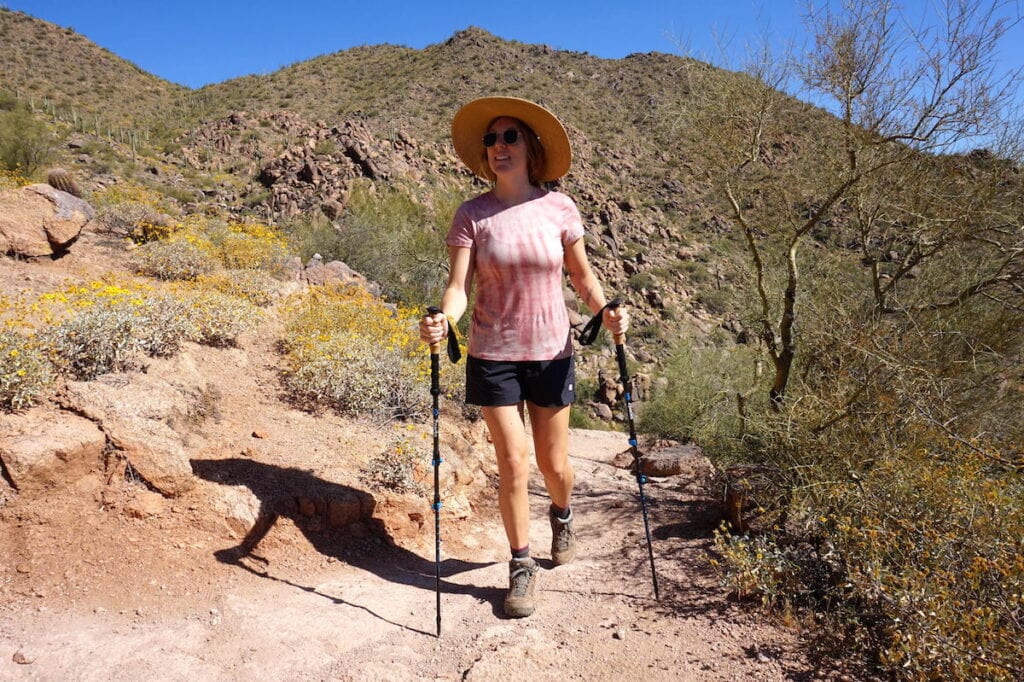 a woman hikes on a trail in Arizona surrounded by desert. She is wearing a Smartwool Merino t shirt and using Zpacks Carbon Fiber trekking poles
