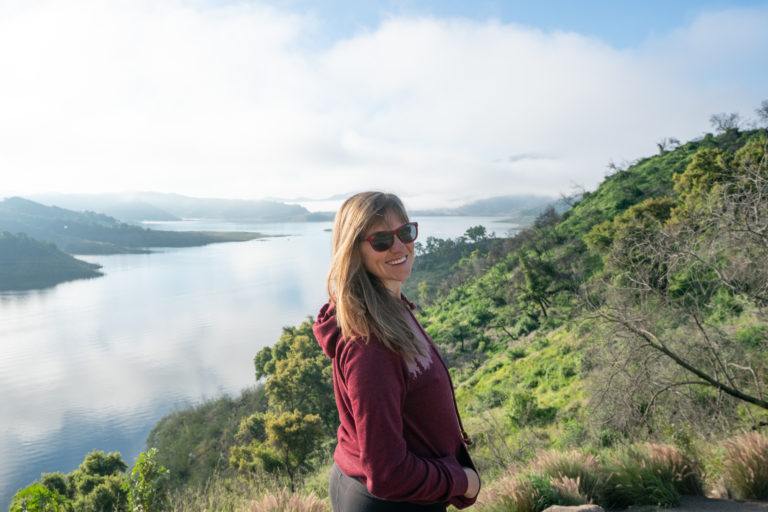 Kristen Bor, founder of Bearfoot Theory, wearing a maroon tentree hoodie while hiking in Central California with the ocean and green hills in the background