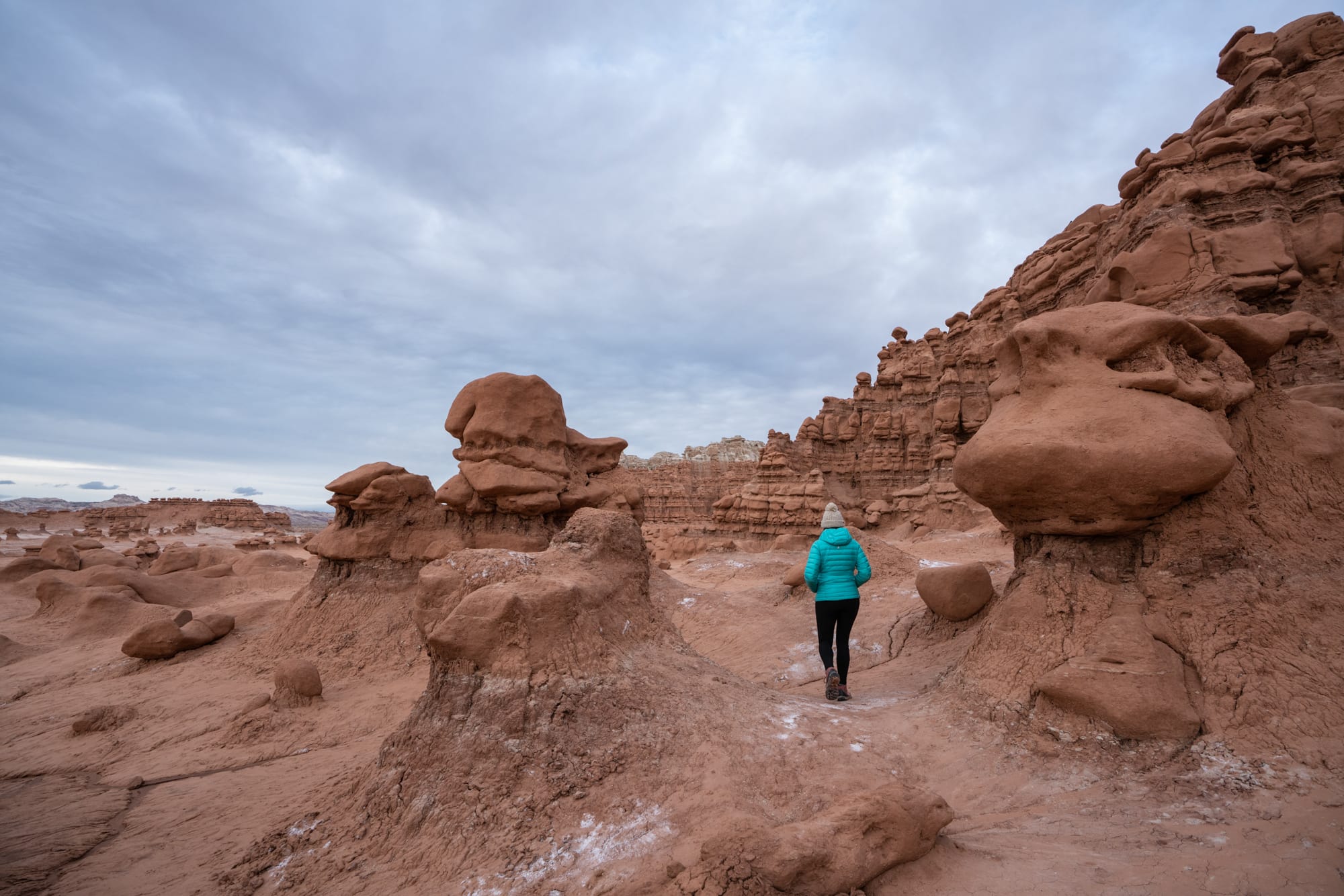 A woman in a blue coat hiking among the goblins in Goblin Valley State Park in Utah