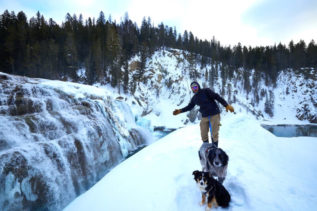 Man and two dogs at the base of Wapta Falls in Yoho National Park on a snowy winter day