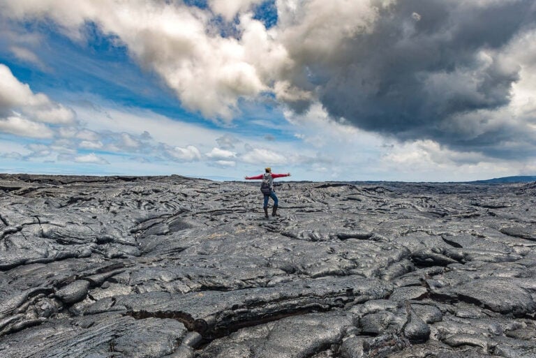 Woman standing with arms outstretched on cold lava field in Hawaii Volcanoes National park