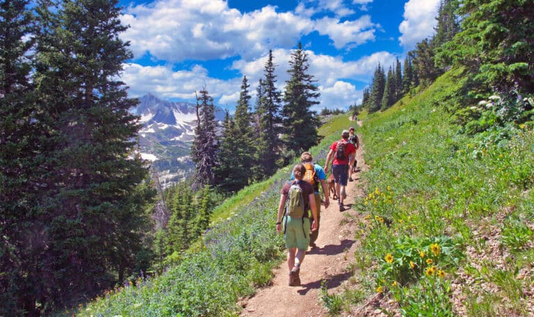 Group of hikers on a trail in Colorado with views of meadows, snow-capped peaks and forest
