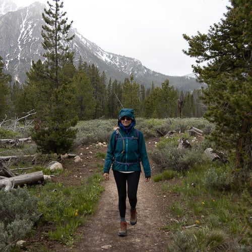 Woman hiking in the rain on a forested trail wearing a hooded rain jacket