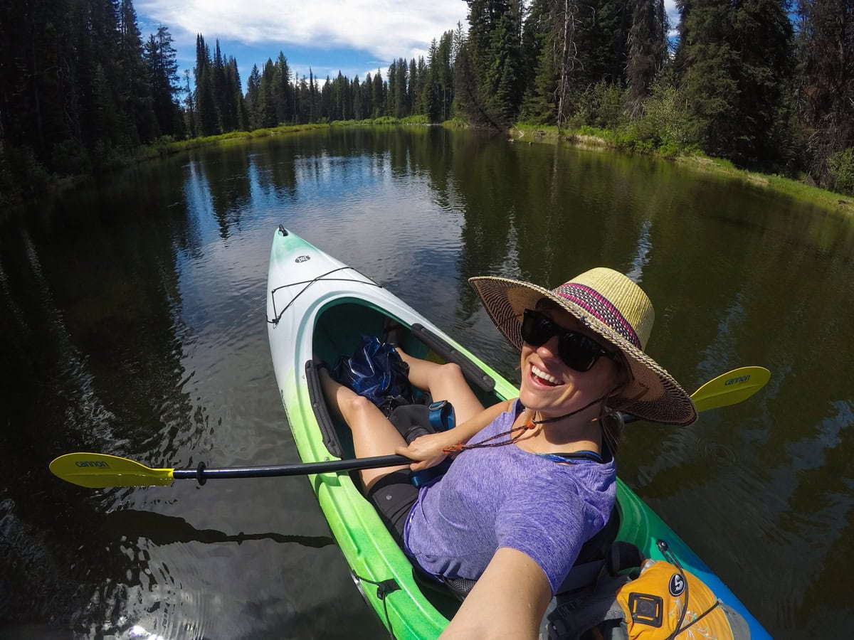 Kristen Bor taking a selfie from a green kayak on a flatwater section of river in McCall Idaho