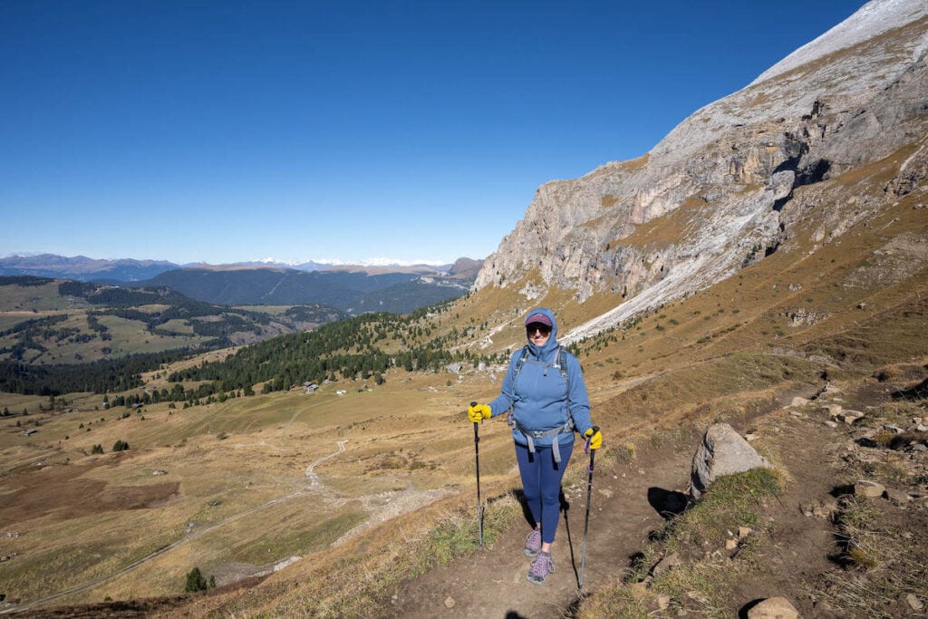 Kristen on hiking trail in Italy using trekking poles and wearing leggings and long-sleeve fleece