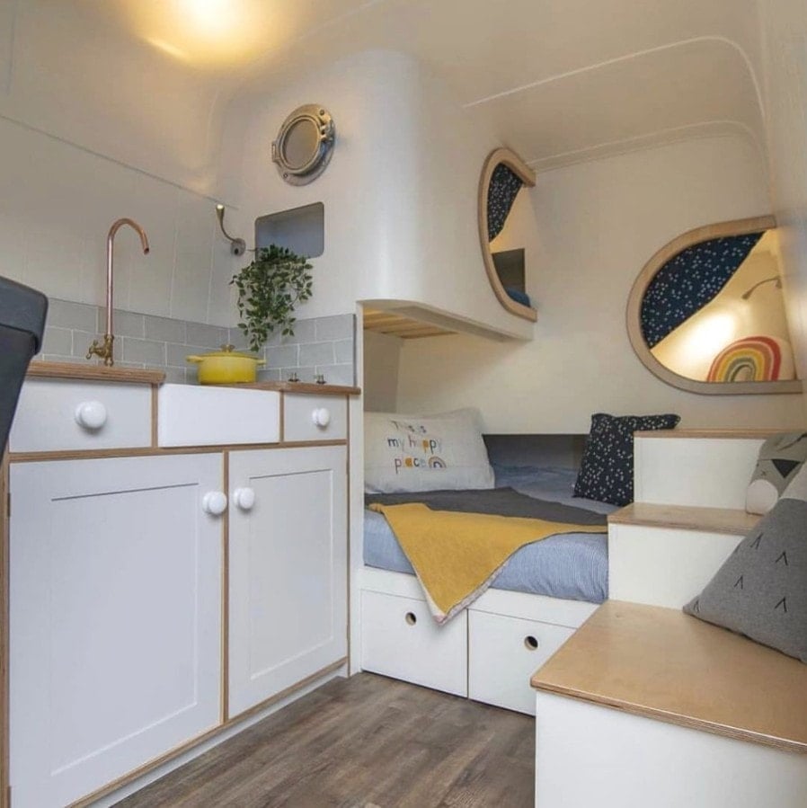 The interior of a family campervan with a small cubby above a full size bed in the back for kids