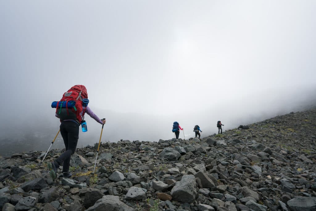 Hikers with backpacking packs hiking up a rocky trail in the fog