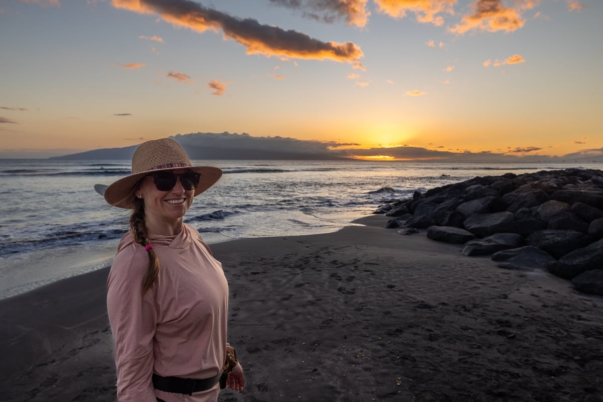 Kristen Bor standing on the beach in Maui at sunset wearing a pink REI Sahara Shade Sun Protection Hoody