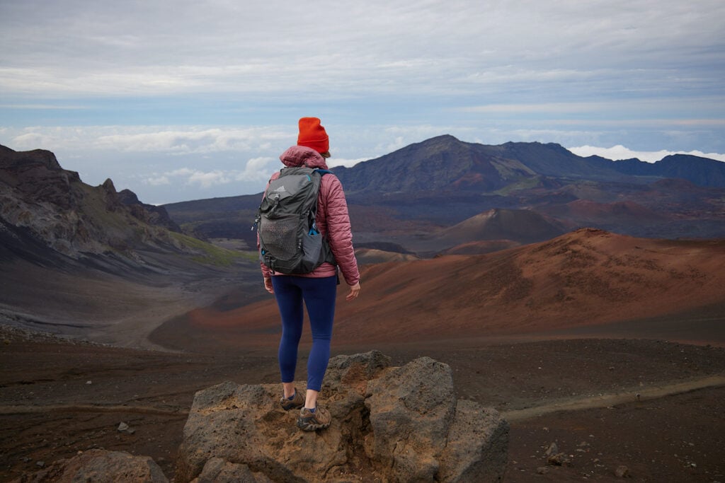 A woman wearing a pink Patagonia Nano Puff Insulated Hoodie on top of Sliding Sands Overlook in Haleakala National Park in Hawaii