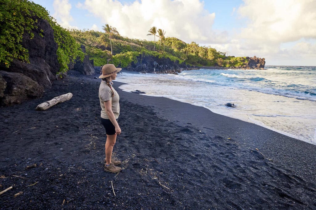 Kristen standing on black sand beach on Maui looking out at ocean