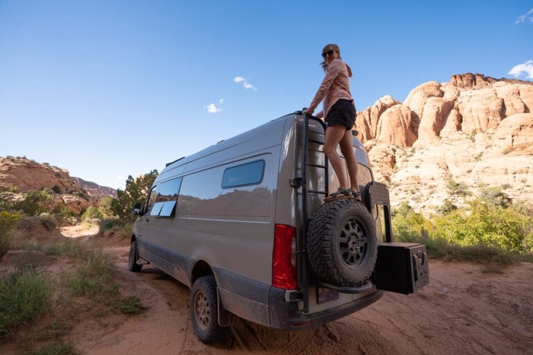 A woman stands on a ladder on the back of her Sprinter van
