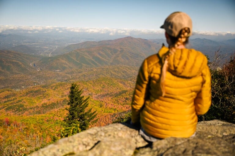 Female hiker facing away from camera sitting on rock viewpoint overlooking Smoky Mountains National Park in fall
