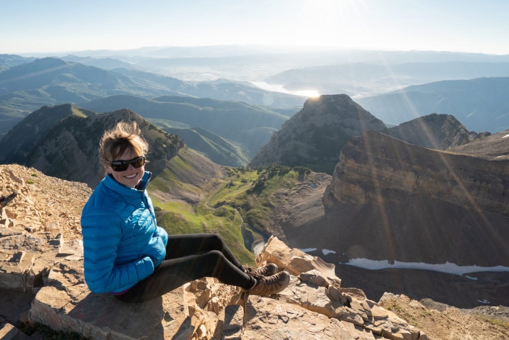 Woman sitting on summit of Mount Timpanogos in Utah with beautiful mountain ridge vista behind her