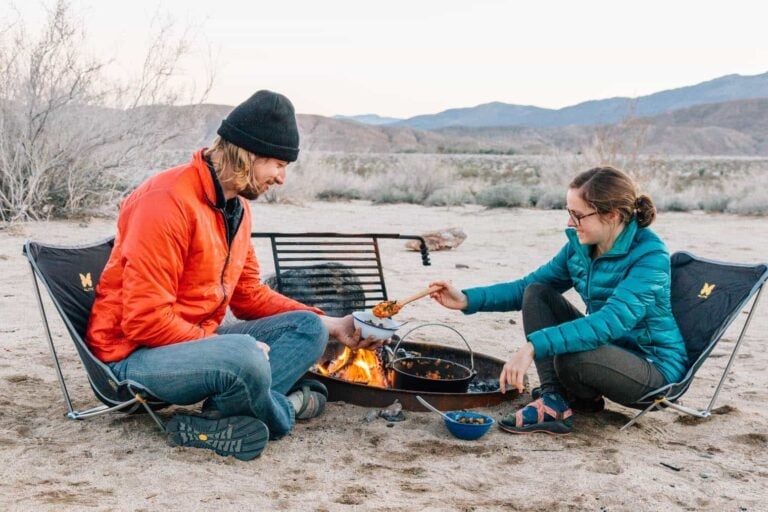 a man and woman cooking over a campfire