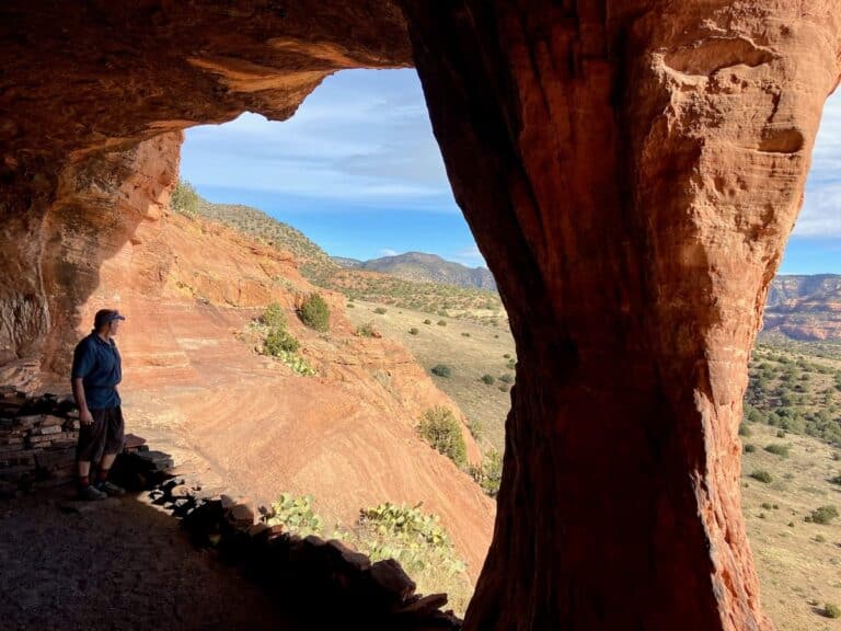 Man standing under archway of cave entrance at Robbers Roost Cave in Sedona