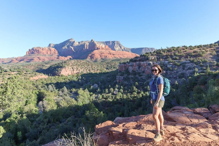 Female hiker standing at lookout on trail in Sedona surrounded by red rock bluffs and forest