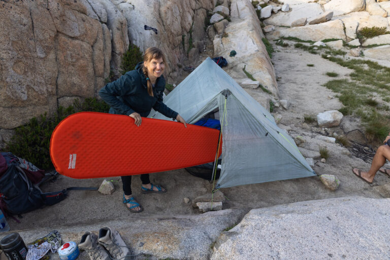 Bearfoot Theory founder Kristen Bor holding a red therm-a-rest prolite plus sleeping pad and putting it into her backpacking tent