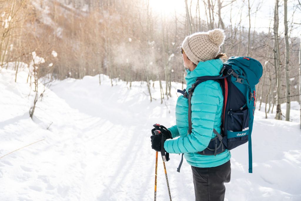 Woman on winter hike wearing gloves, a teal puffy, hat and a backpack