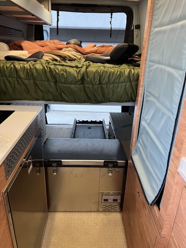 Interior of a Sprinter Van. Photo shows a National Luna Fridge underneath a platform bed