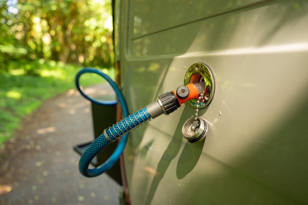 A close up of a blue hose refilling the water tank of a Sprinter camper van