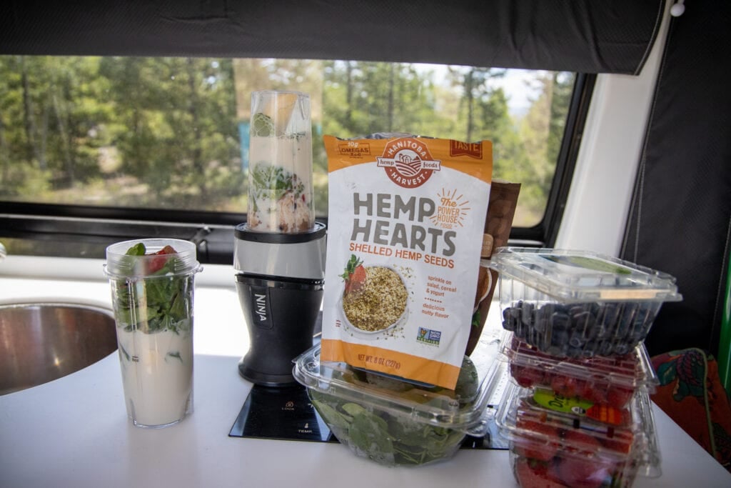 Smoothie ingredients sitting on the countertop inside of a Sprinter Van. There is a small Ninja blender and 3 plastic crates of berries.