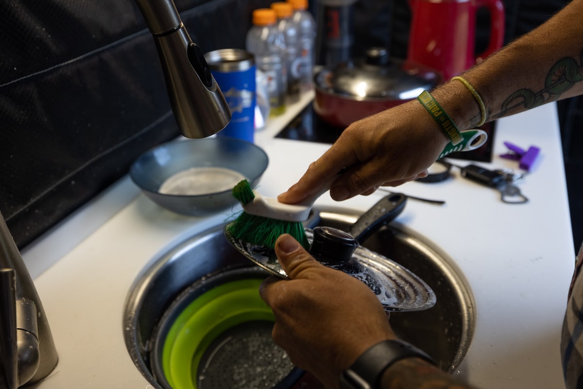 Two hands scrubbing a dish with a brush in the sink of a van