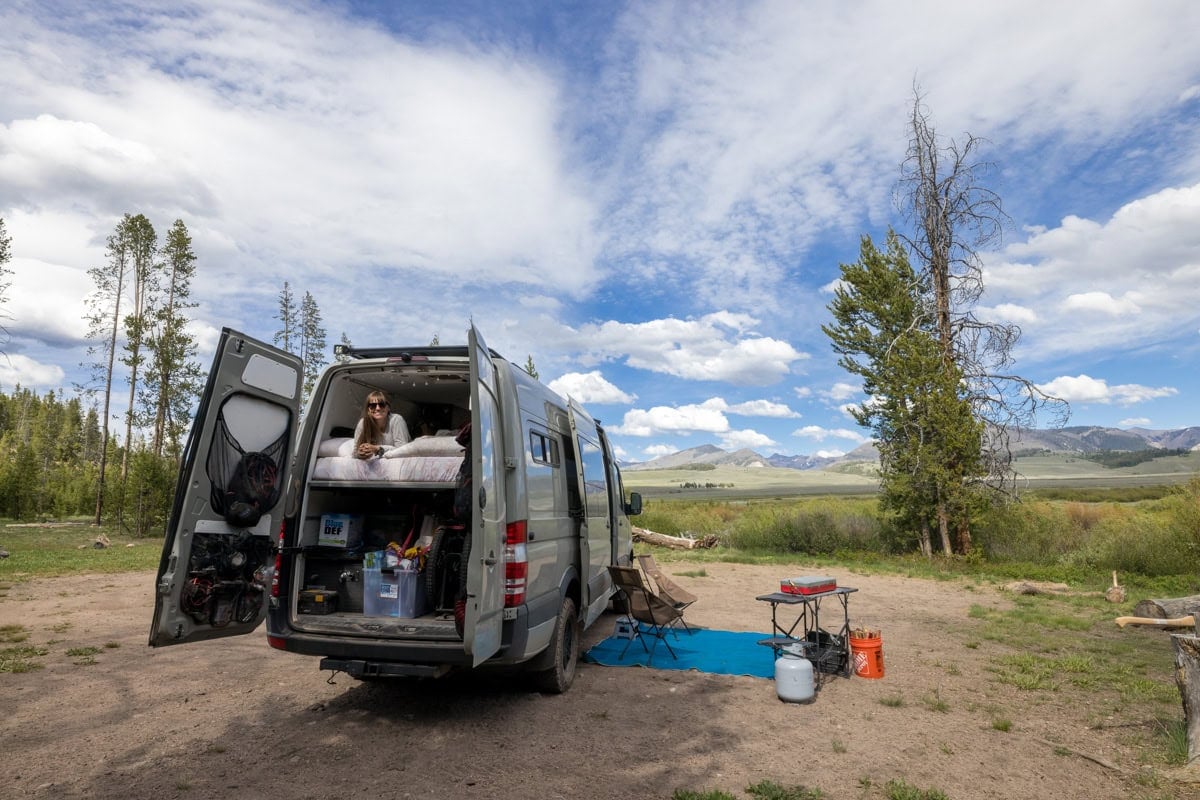 Kristen Bor lying in the bed of a Sprinter Van looking out the back doors at a dispersed campsite in Stanley Idaho