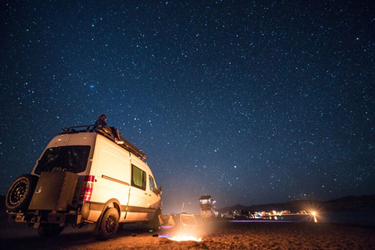 Sprinter Van and many other vehicles camped on the beach at night under a starry sky at Lone Rock on Lake Powell