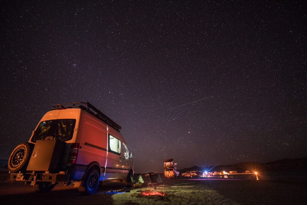 Sprinter Van and many other vehicles camped on the beach at night under a starry sky at Lone Rock on Lake Powell