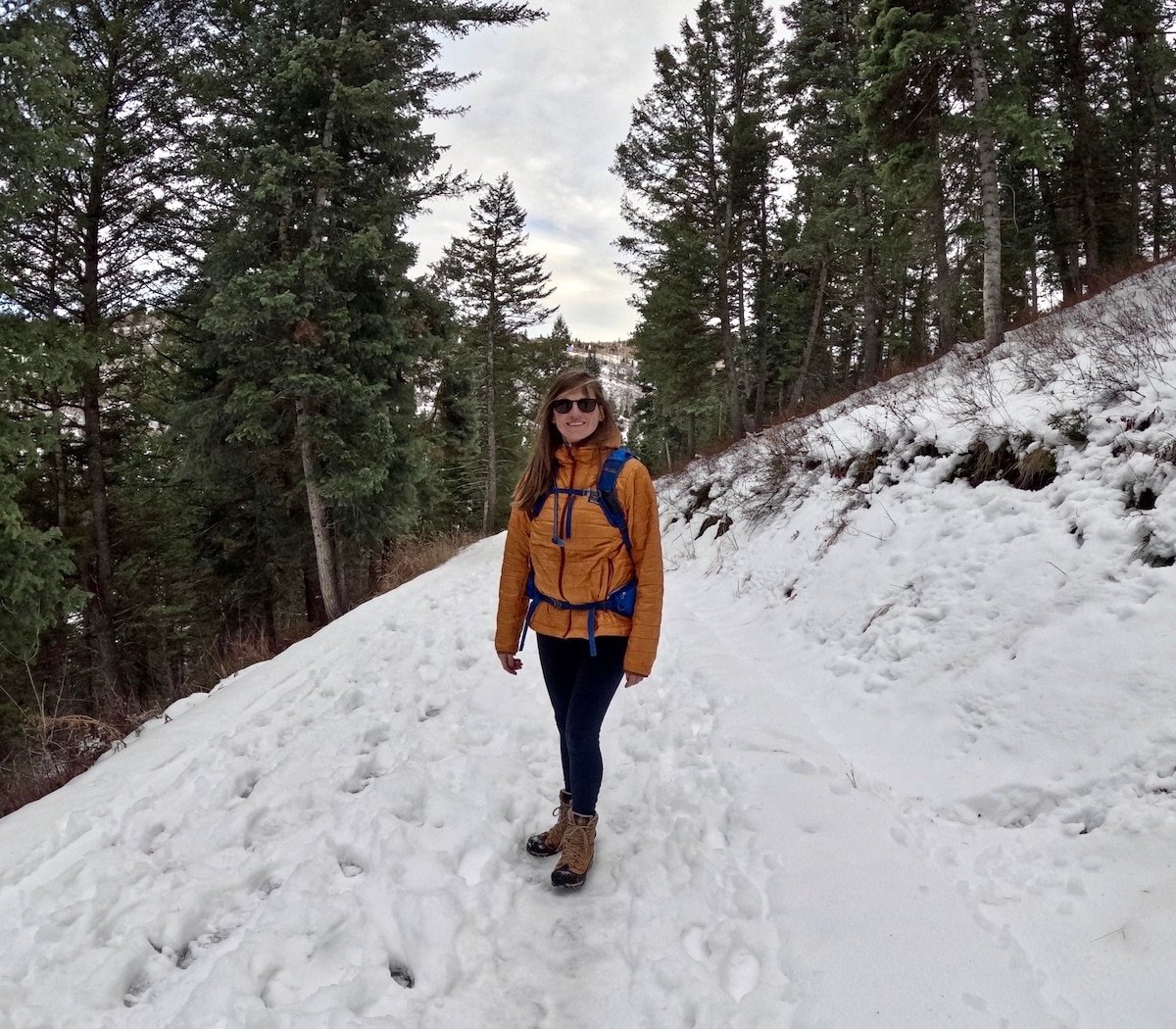 Kristen Bor in a Patagonia Nano Puff in Utah Park surrounded by trees, snow, and a cloudy sky