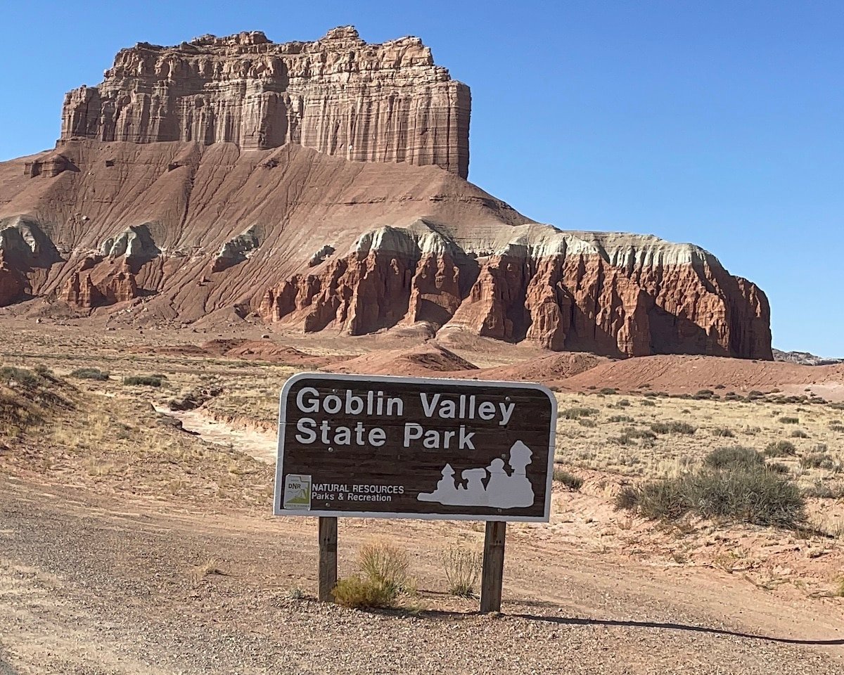 Entrance sign for Goblin Valley State Park in Utah with an orange rock feature behind it