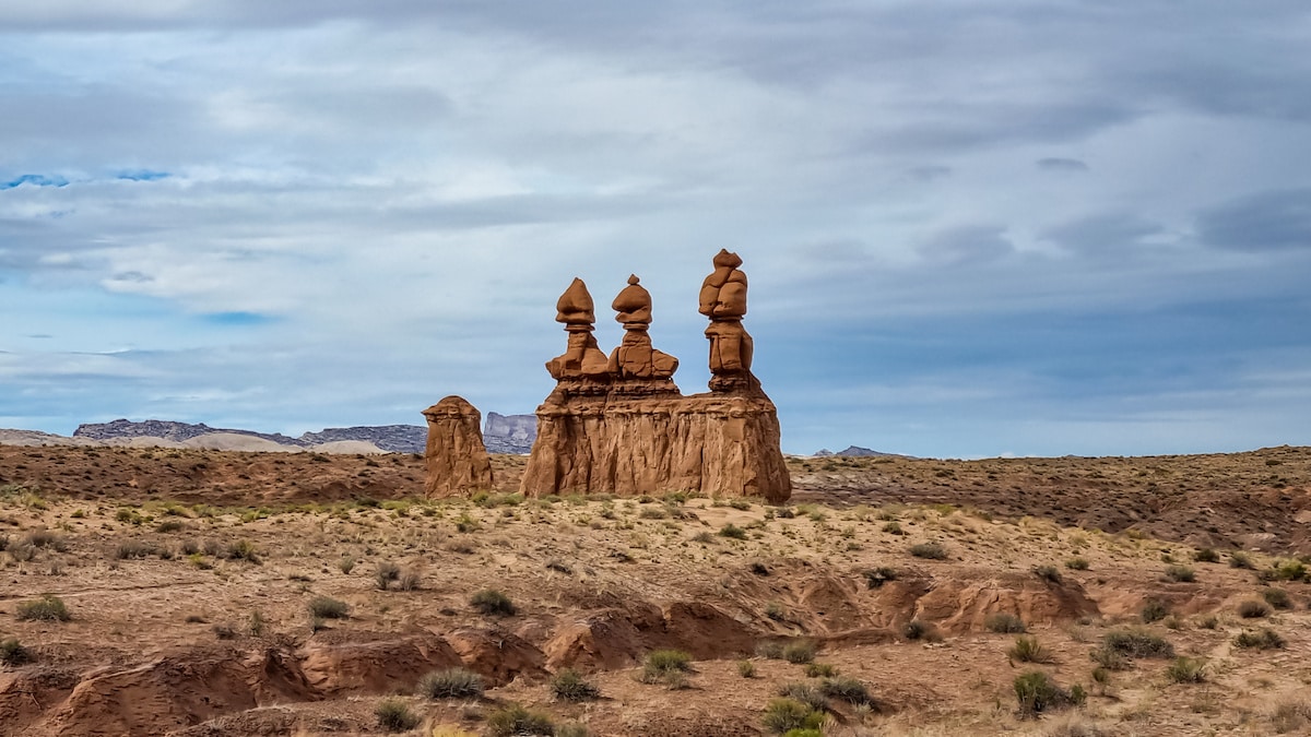 Three Sisters rock formation consisting of three tall hoodoo spires on a cloudy day in Goblin Valley State Park in Utah