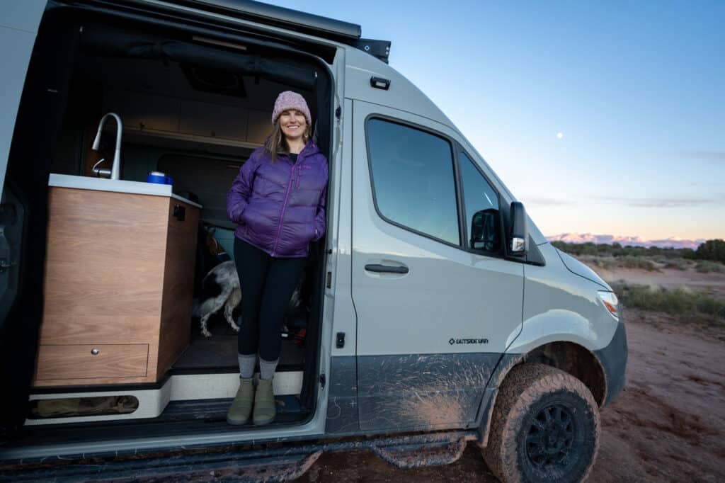 Bearfoot Theory founder Kristen Bor standing in the doorway of her Sprinter camper van in Moab Utah at sunset