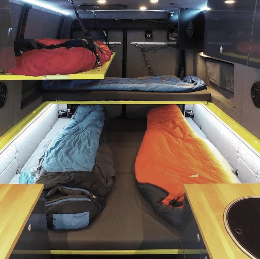Two kids fold out beds above a full size bed in a campervan