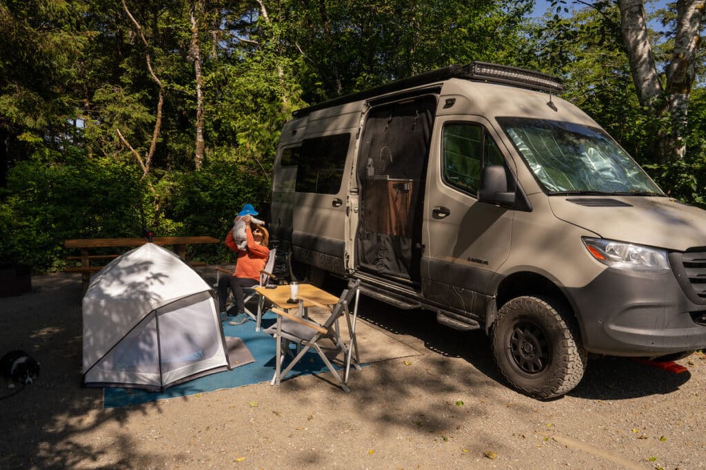 Bearfoot Theory founder Kristen Bor sitting next to her Sprinter Van at a campsite holding her baby