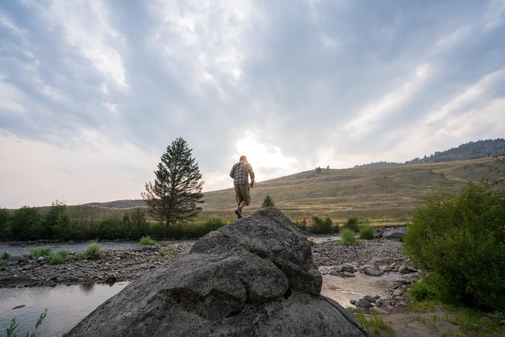 Man standing on a rock rock overlooking a river in Slough Creek in Yellowstone National Park