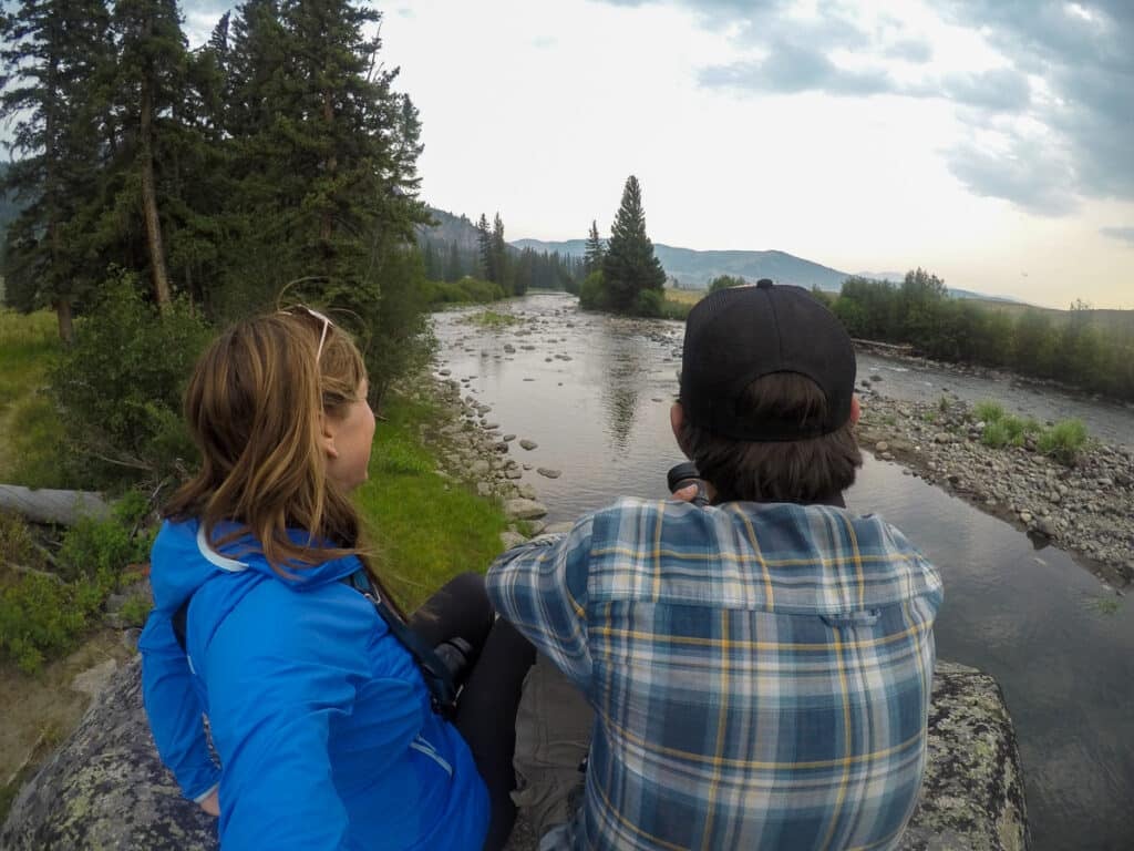 Two people sitting on a rock overlooking a river in Slough Creek in Yellowstone National Park